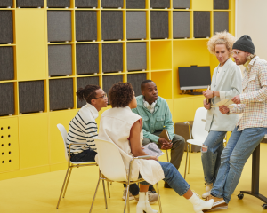 Group of diverse young adults brainstorming sitting in circle, in a yellow room