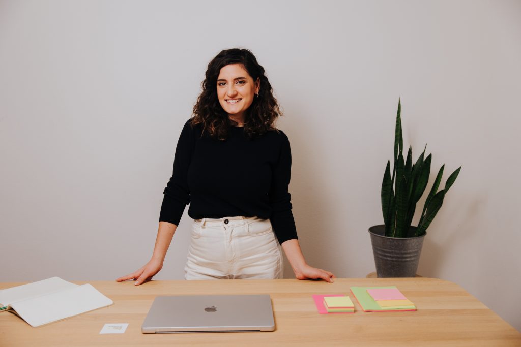 Woman smiling standing between wall and desk - startup judge and startup recruitment expert